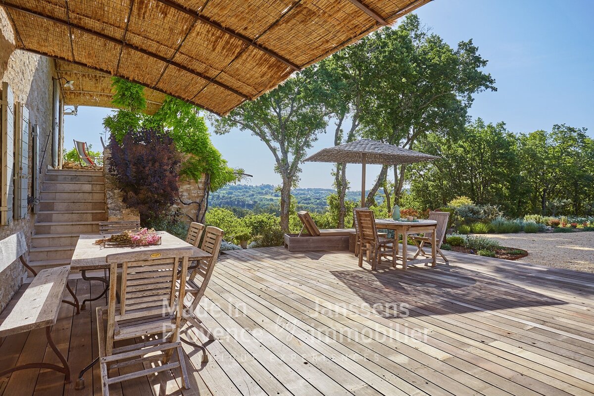 A wooden deck with a table and chairs under a thatched roof