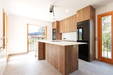 Bright modern kitchen with wood cabinets, a large island, black appliances, and big windows offering a scenic view.