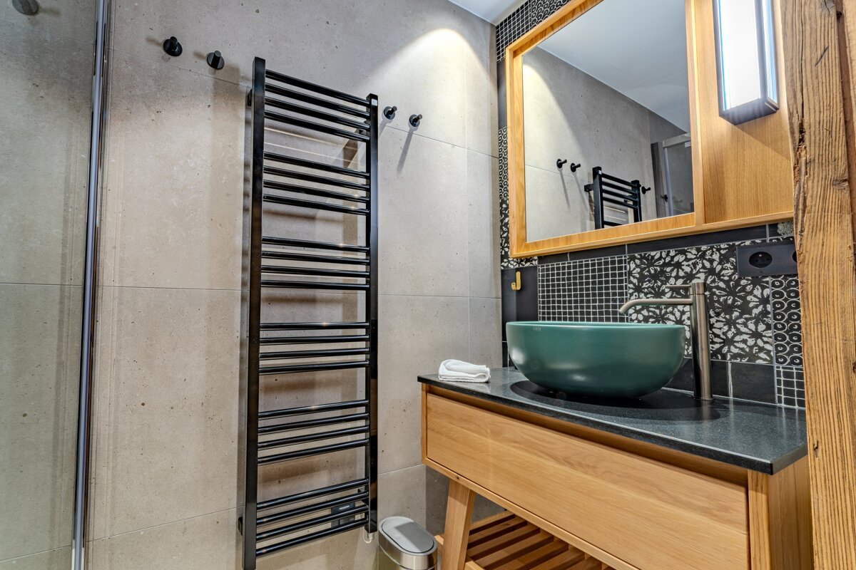 Modern bathroom with a black towel warmer, green bowl sink on a wooden vanity, and patterned black and white tiles.