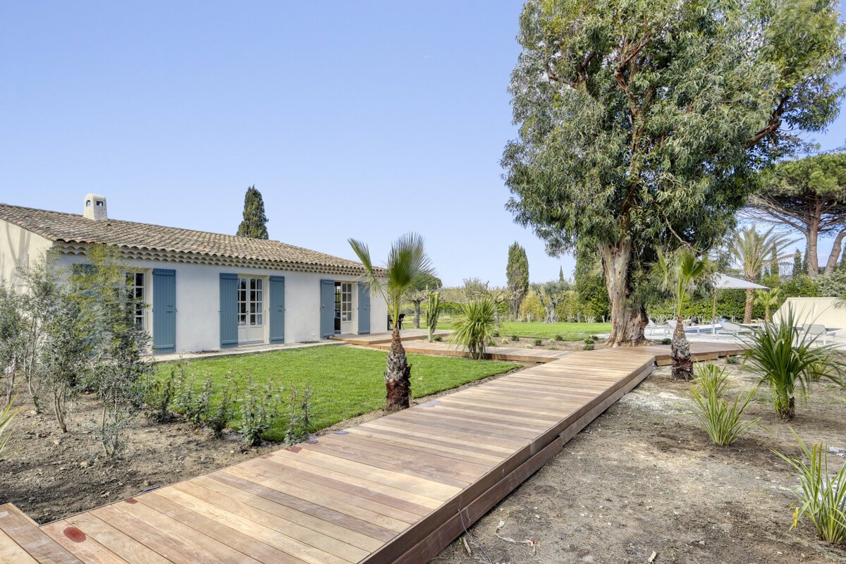 A wooden walkway leads to a white house with blue shutters