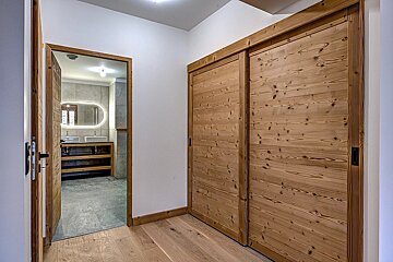 Hallway with rustic wooden sliding doors leading to a modern bathroom with double sinks and a backlit oval mirror.