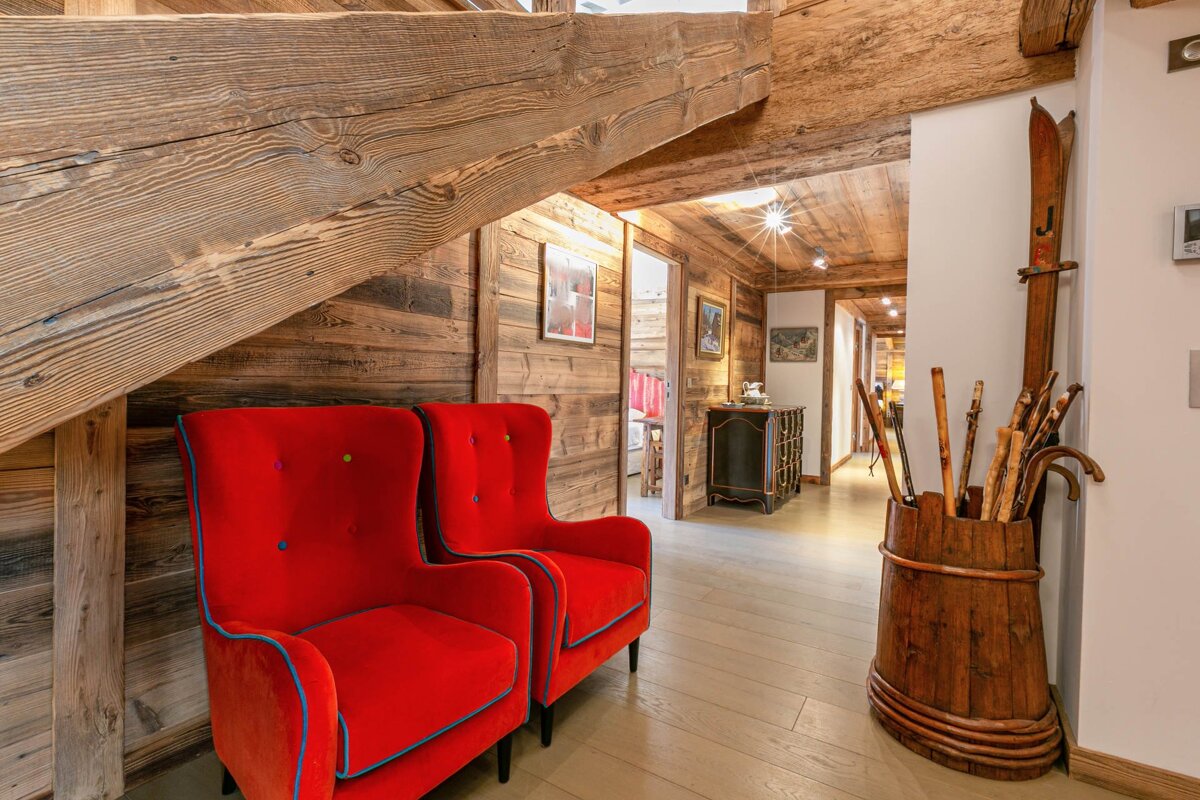 Two bright red armchairs under a rustic wooden staircase in a cozy, wood-paneled chalet interior with ski decor.