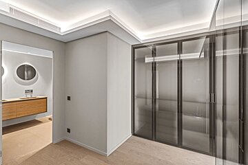 Modern hallway with glass-door wardrobes and an adjacent bathroom featuring a floating wooden vanity and round mirror.
