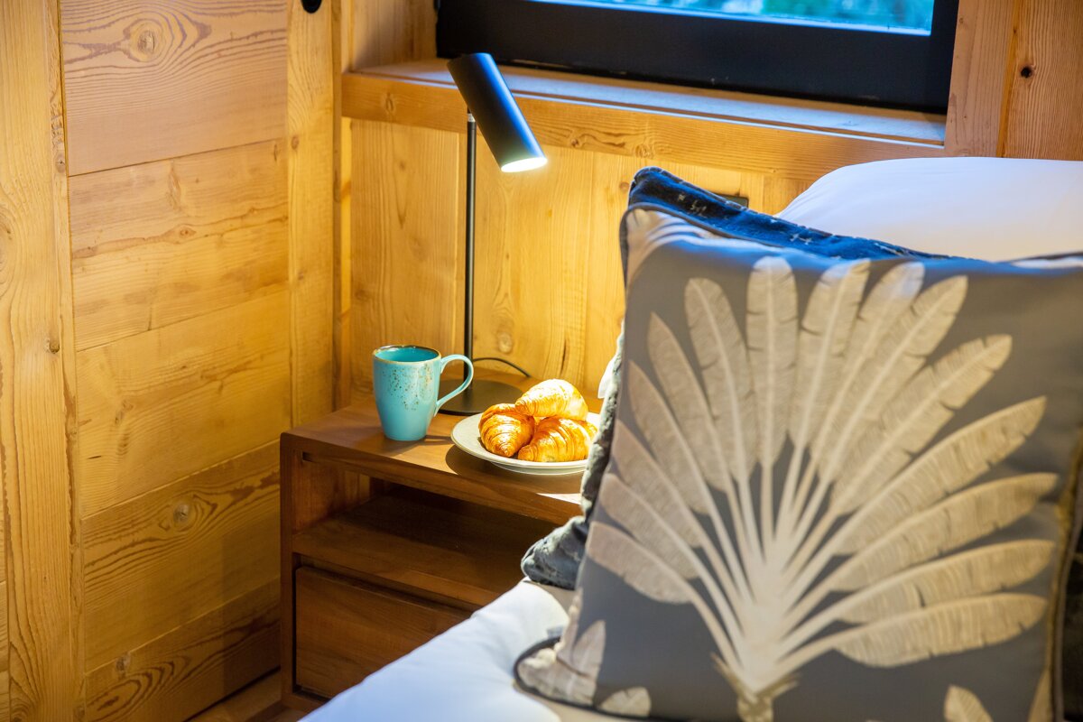 A nightstand with a plate of croissants and a blue mug on it