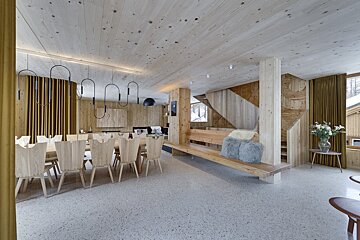 Modern wooden chalet interior featuring a large dining table, light pine paneling, terrazzo floors, and minimalist black light fixtures.