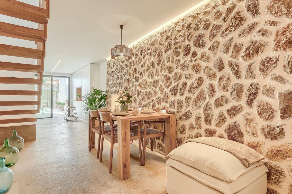 A chic dining area showcases a textured stone wall, wooden dining table, and sleek open wooden staircase, blending natural elements with modern design.