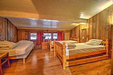 A cozy, rustic bedroom with wood-paneled walls, a low ceiling, and three single beds.