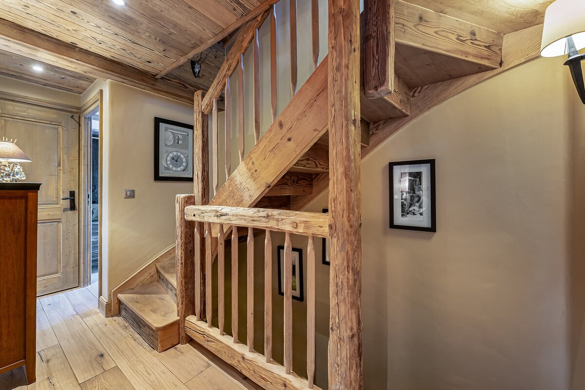 A rustic wooden staircase, railing, ceiling, and floor create a cozy, chalet-style interior with beige walls displaying framed art.