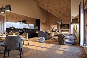 Modern open-concept living room and kitchen featuring warm wood panels, textured grey seating, and cozy lighting.