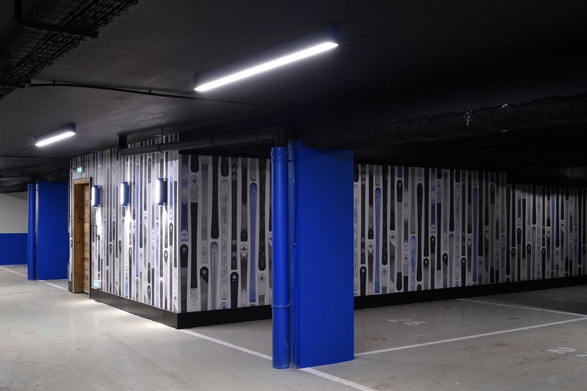 Modern underground parking with ski-themed walls, bright blue accents, black ceiling lights, and concrete floor with parking lines.