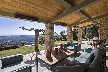 A luxurious covered patio with stone pillars, comfortable seating, and a breathtaking panoramic view of the rolling hills and sea.