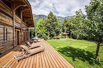 A wooden deck with chairs and mountains in the background
