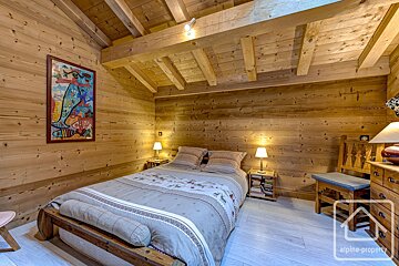 Chalet-style bedroom entirely clad in wood, featuring a double bed, bedside lamps, and a colorful artwork.
