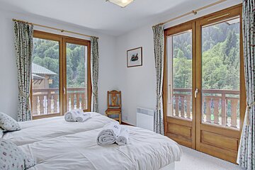 A bedroom with two beds and a balcony with trees in the background