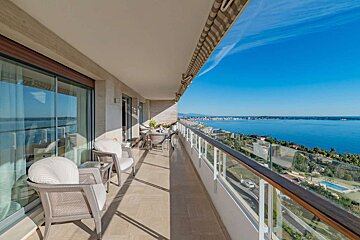 Spacious balcony with outdoor seating and stunning panoramic views of the blue sea, coastline, and sky on a sunny day.