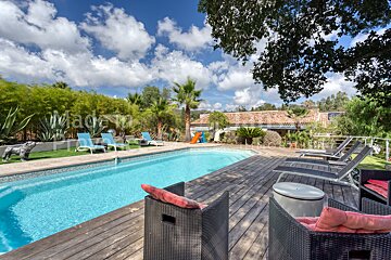 A large swimming pool is surrounded by chairs and a wooden deck