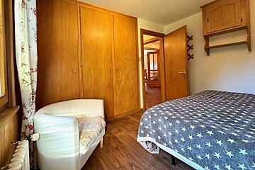 A cozy bedroom featuring large wooden closets, a white armchair, and a bed with a star-patterned blanket.
