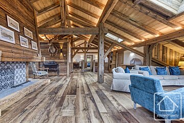 A vast, rustic wooden living room with exposed beams, a tiled fireplace, deer taxidermy, and comfortable sofas with blue cushions.