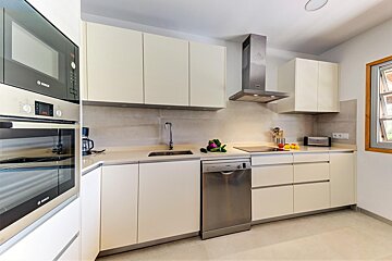 A sleek, modern kitchen with cream cabinets, stainless steel oven, microwave, dishwasher, and range hood. A sink, cooktop, and window complete the bright space.