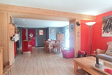 A vibrant open-plan chalet interior with natural wood accents, bold red walls, a dining area with a long table, and a cozy living space.