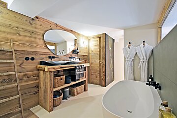 A rustic-modern bathroom with wood paneling, double vessel sinks, an oval mirror, and a sleek white freestanding tub, evoking a chalet feel.