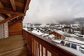 View from a wooden balcony overlooking a snowy alpine village under a cloudy, misty sky.