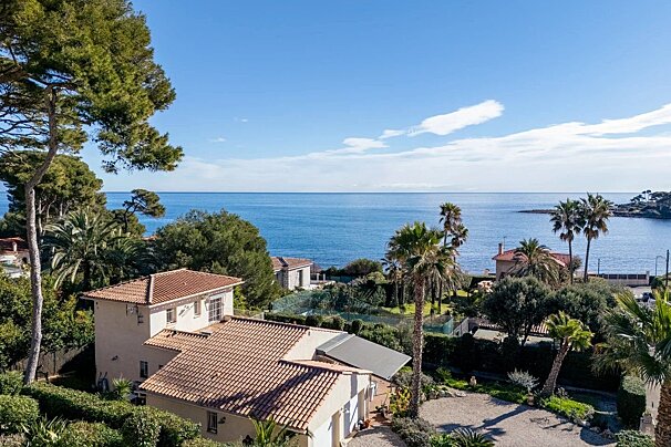 Beautiful Mediterranean coastal view with tiled-roof villas and palm trees overlooking the calm blue ocean.