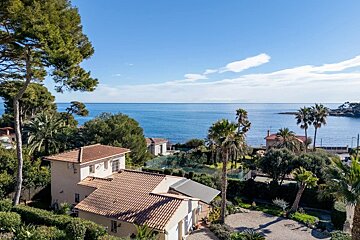 Beautiful Mediterranean coastal view with tiled-roof villas and palm trees overlooking the calm blue ocean.