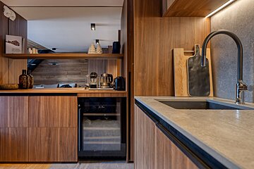 A modern kitchen area features sleek wood cabinetry, concrete countertops, a black faucet over the sink, a built-in wine cooler, and a coffee setup.