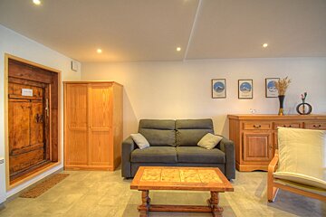 A simple, well-lit living room with a dark sofa, wooden storage, a rustic door, and decorative pictures on bright white walls.