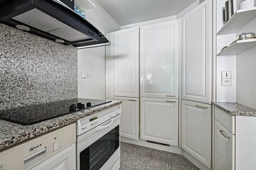 A modern white kitchen with speckled granite countertops and backsplash, black induction hob, oven, dishwasher, and glossy white cabinets.