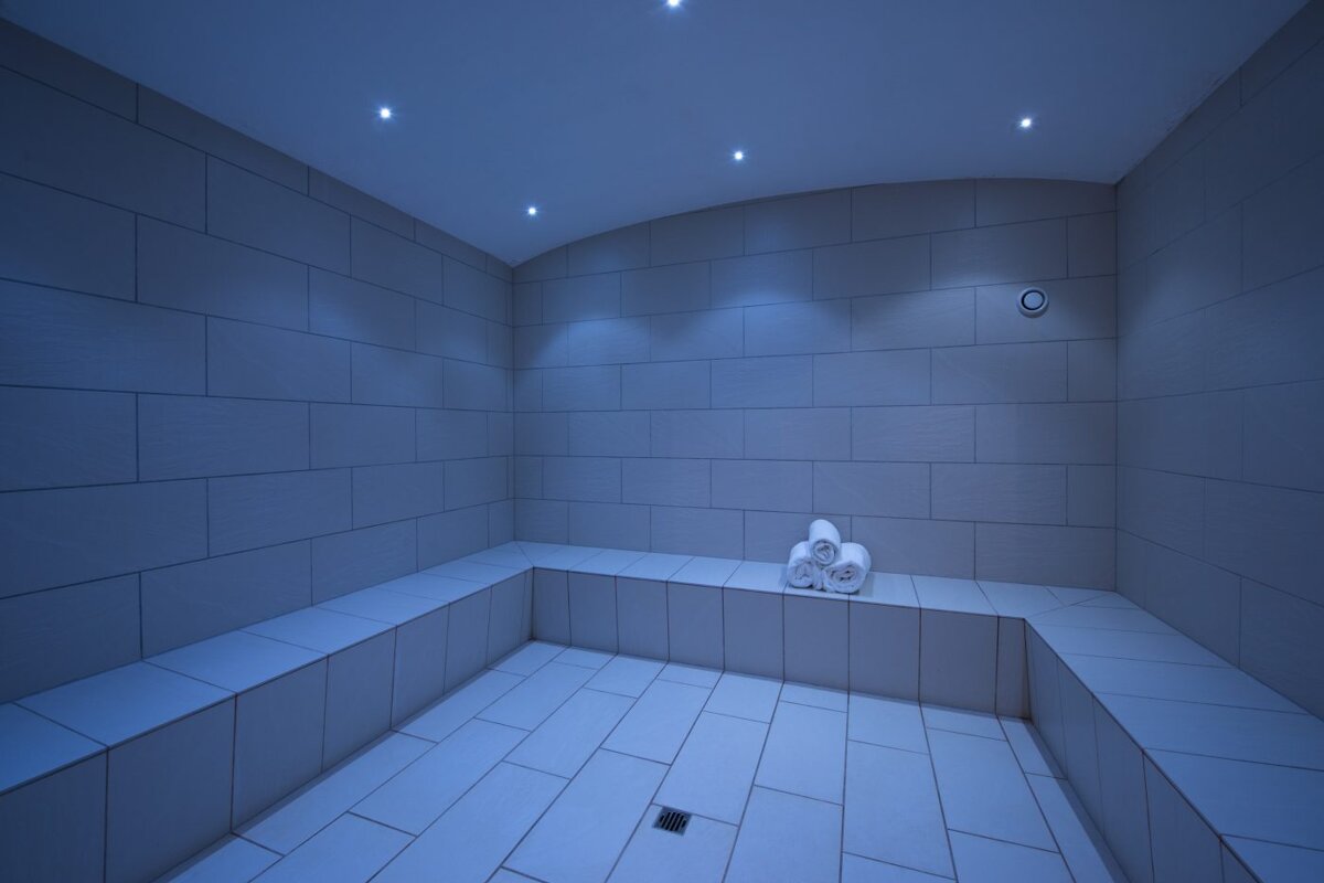 A room with white tiles and a few towels on a bench