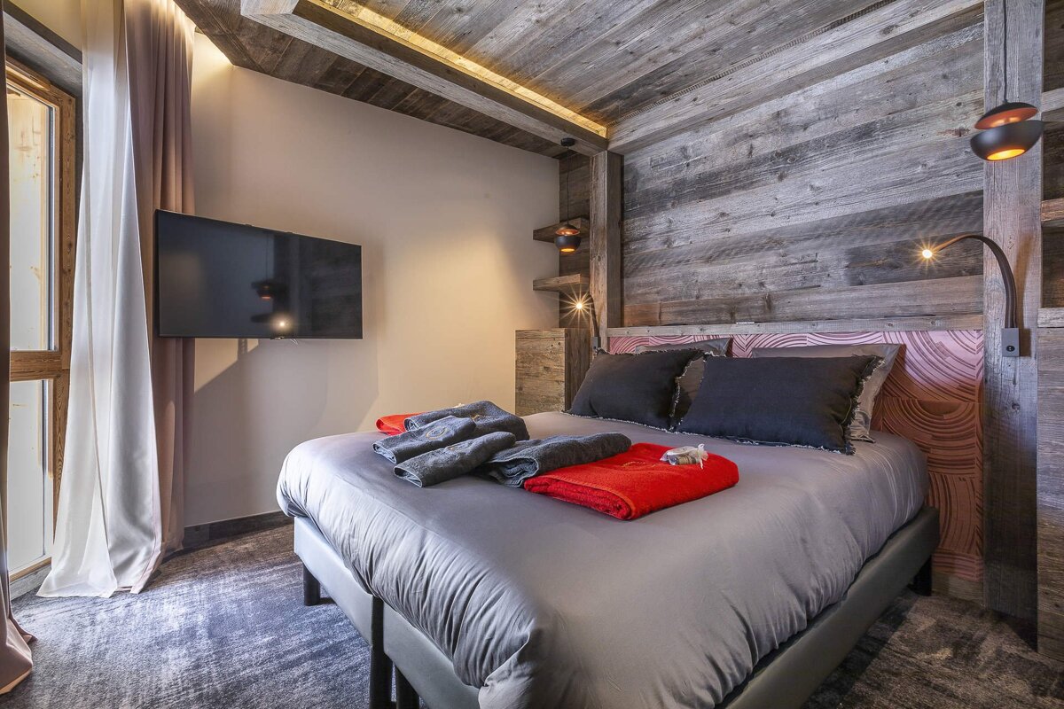 Cozy rustic bedroom featuring a wood-paneled accent wall, a bed with grey linens, and a wall-mounted TV.