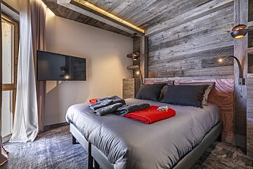 Cozy rustic bedroom featuring a wood-paneled accent wall, a bed with grey linens, and a wall-mounted TV.