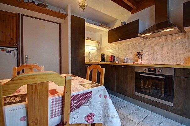 A functional kitchen with a dining table in the foreground, featuring dark brown cabinets, a tiled backsplash, and modern appliances like an oven.
