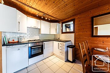 A cozy kitchen with modern white cabinets, subway tile backsplash, and appliances, contrasted with warm wood-paneled walls and ceiling. A dining area is partly visible.