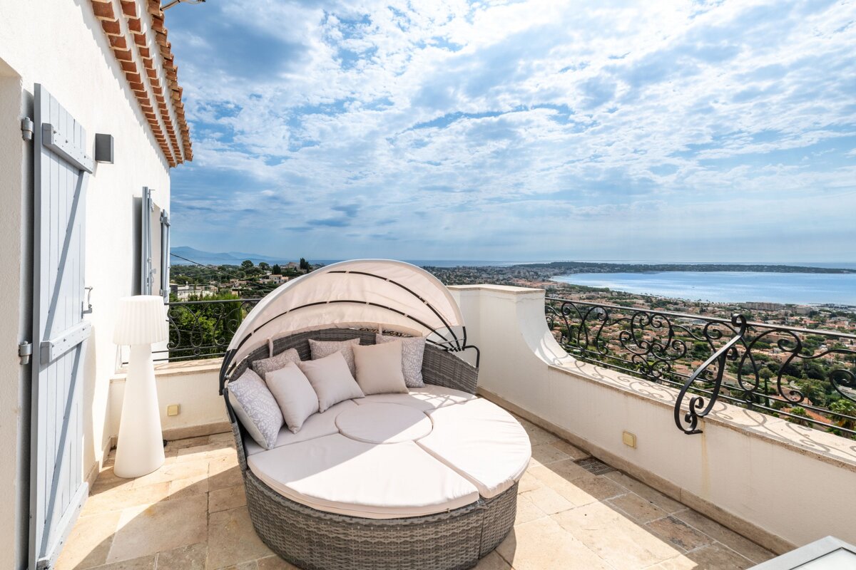 A round couch with a canopy sits on a balcony overlooking the ocean