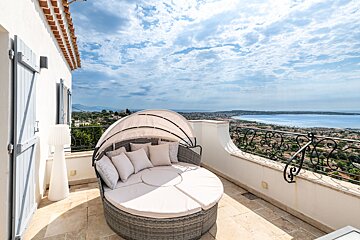 A round couch with a canopy sits on a balcony overlooking the ocean