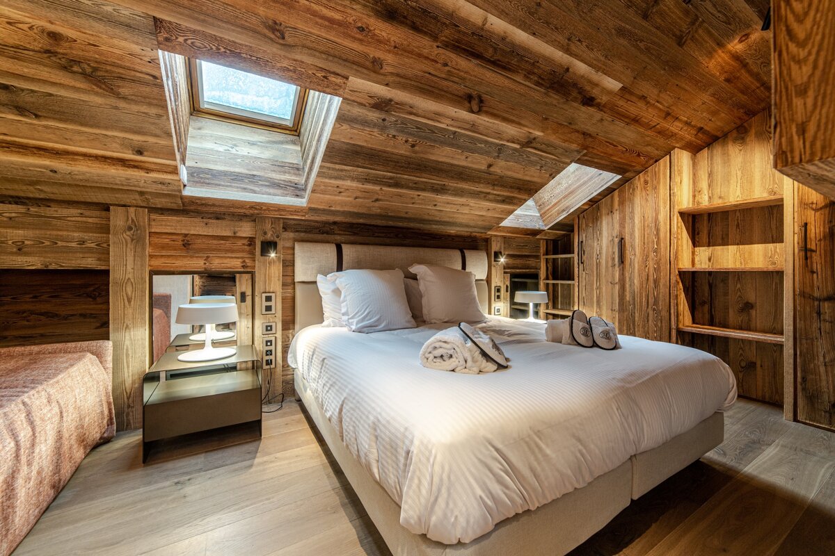 Cozy, rustic chalet bedroom featuring extensive wood paneling, a large bed with crisp white linens, and two skylights.