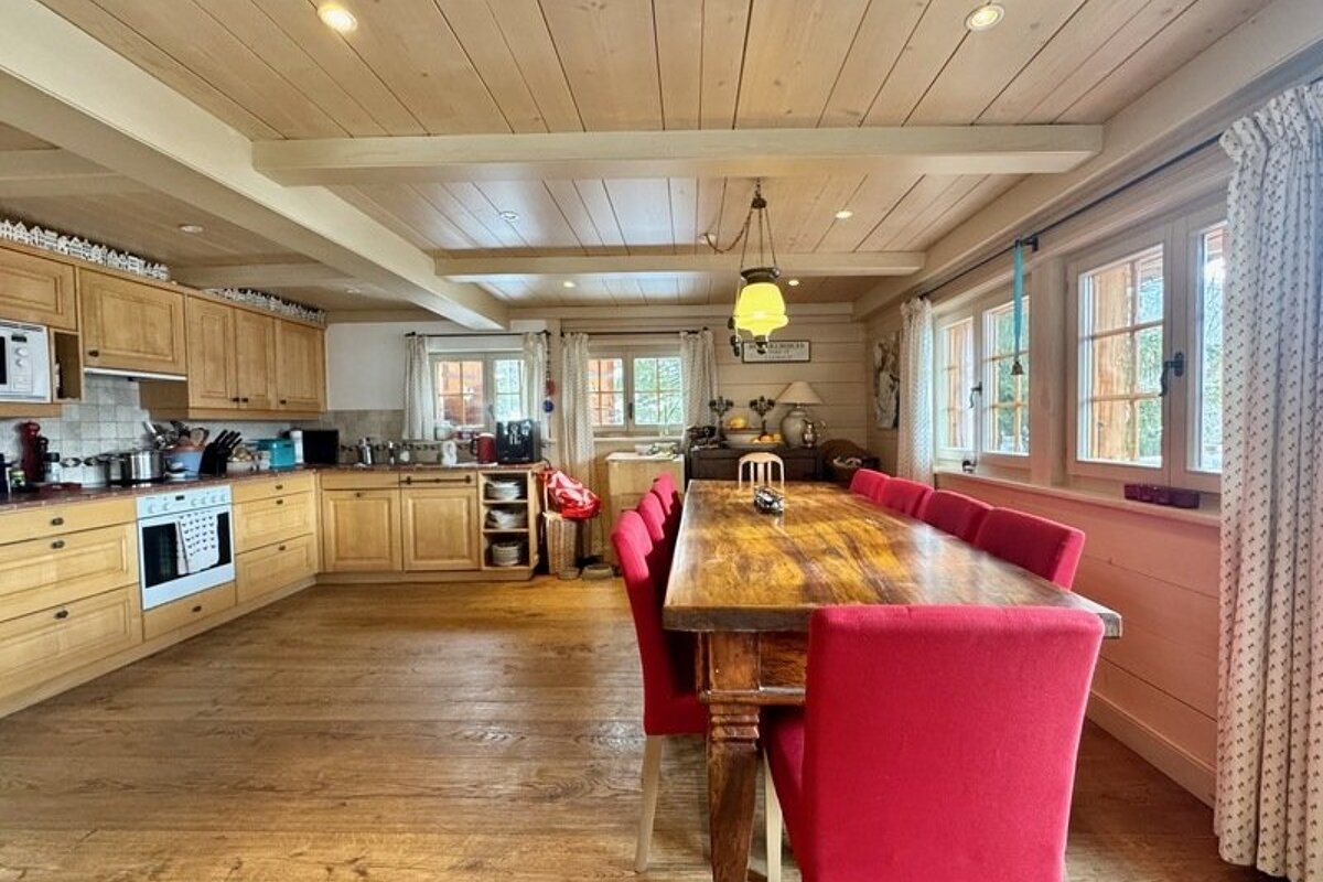 A cozy cabin kitchen and dining area featuring light wood cabinetry, a long wooden table, and vibrant pink upholstered chairs.
