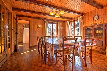 Rustic dining room with wood paneling on walls and ceiling, a long table, tiled floor, and natural light from windows.