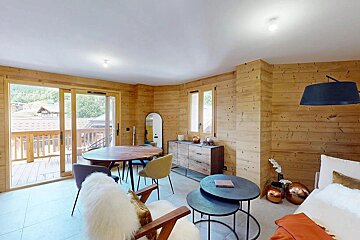 A modern, wood-paneled room with a dining area, contemporary furniture, and a large sliding door opening to a balcony with scenic views.