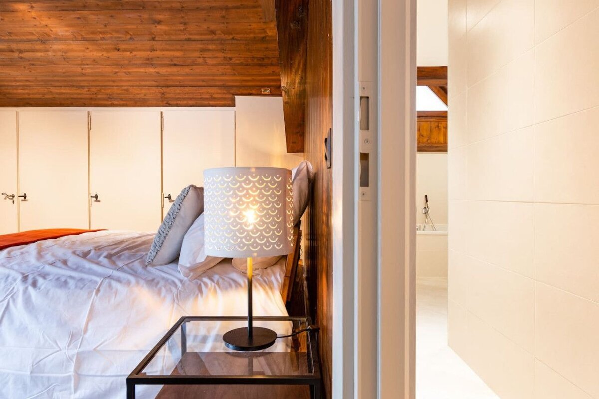 A bedroom with a lamp on a nightstand next to a bed