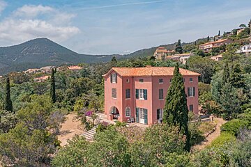 A large pink house is surrounded by trees and mountains