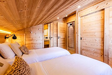 Cozy wooden cabin bedroom with two twin beds, white bedding, leopard-print pillows, and slanted wood ceilings.