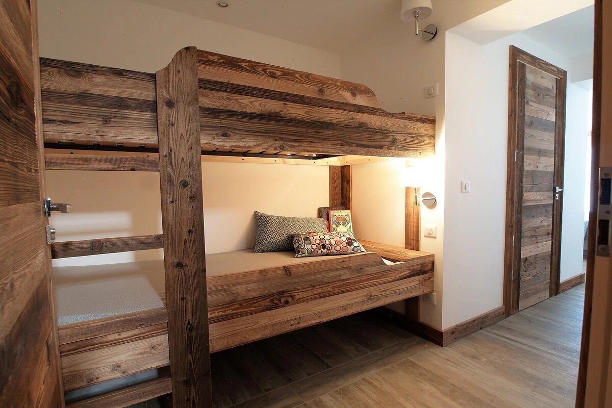 A cozy room features rustic wooden bunk beds with integrated lighting, a wooden door, and matching floor. Warm, natural aesthetic.