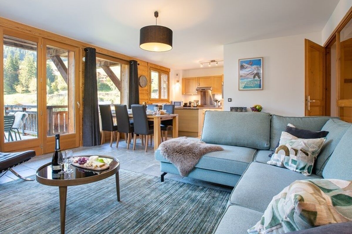 Cozy cabin living room with a light blue sectional, coffee table, dining area, and large glass doors looking outside.