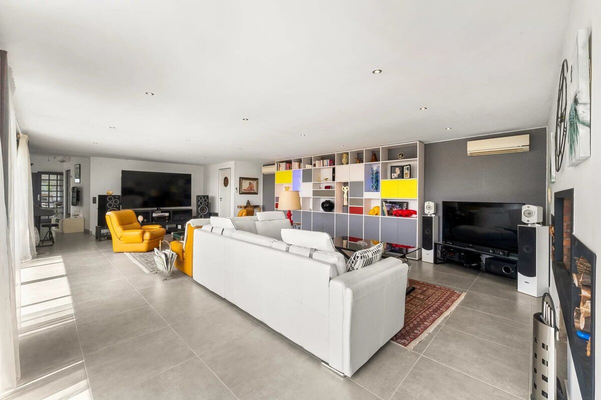 Spacious, modern living room featuring a white sofa, yellow armchairs, large TV, and a vibrant modular shelf.