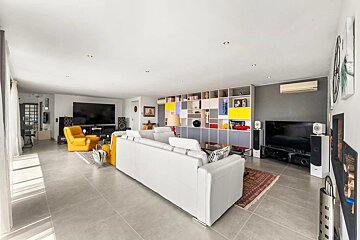 Spacious, modern living room featuring a white sofa, yellow armchairs, large TV, and a vibrant modular shelf.