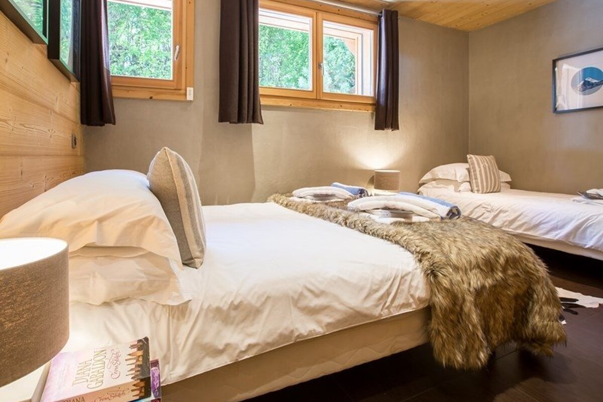Cozy rustic bedroom featuring a large bed with a fur throw, a smaller bed, wood-framed windows, and warm lighting.